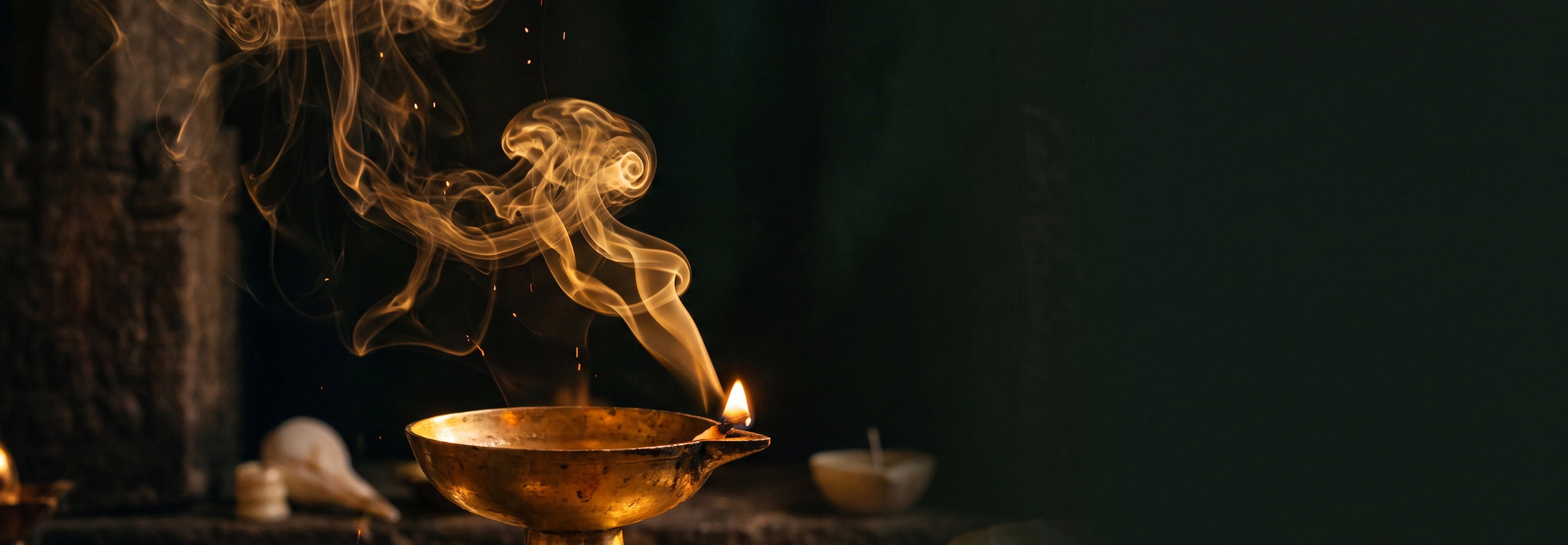 Golden aromatic smoke rising from a lit brass diya lamp in darkness