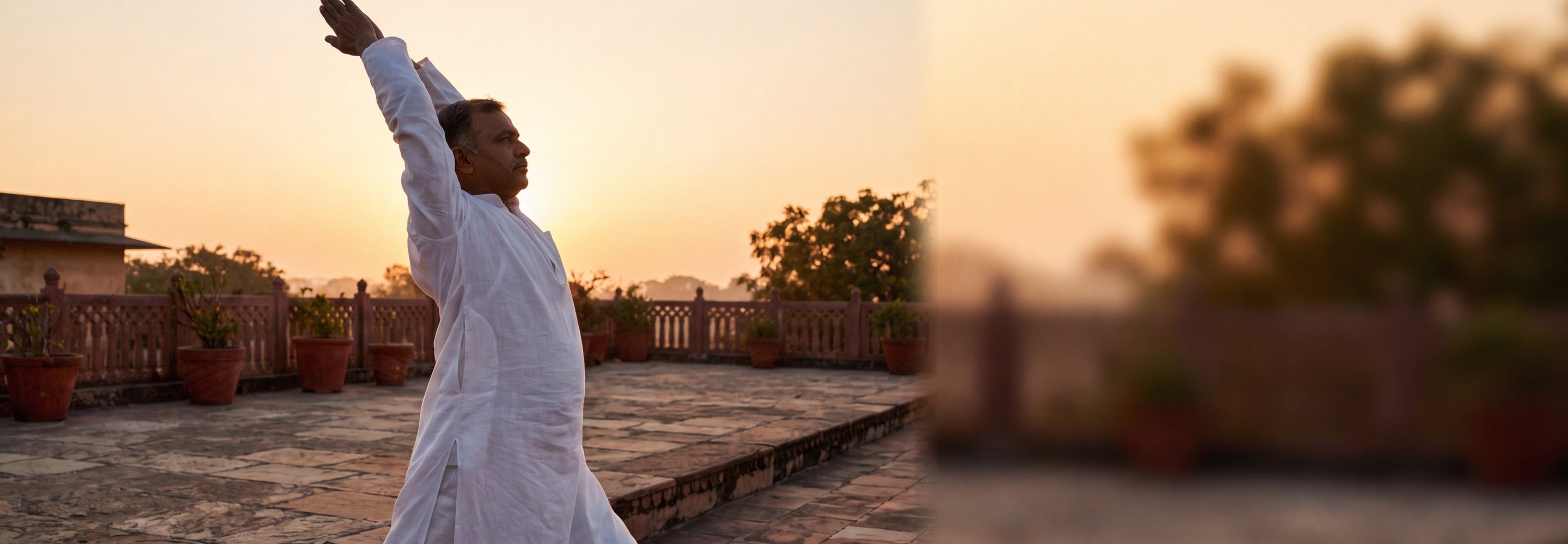 Man in a white kurta seated in a yoga posture outdoors at sunrise